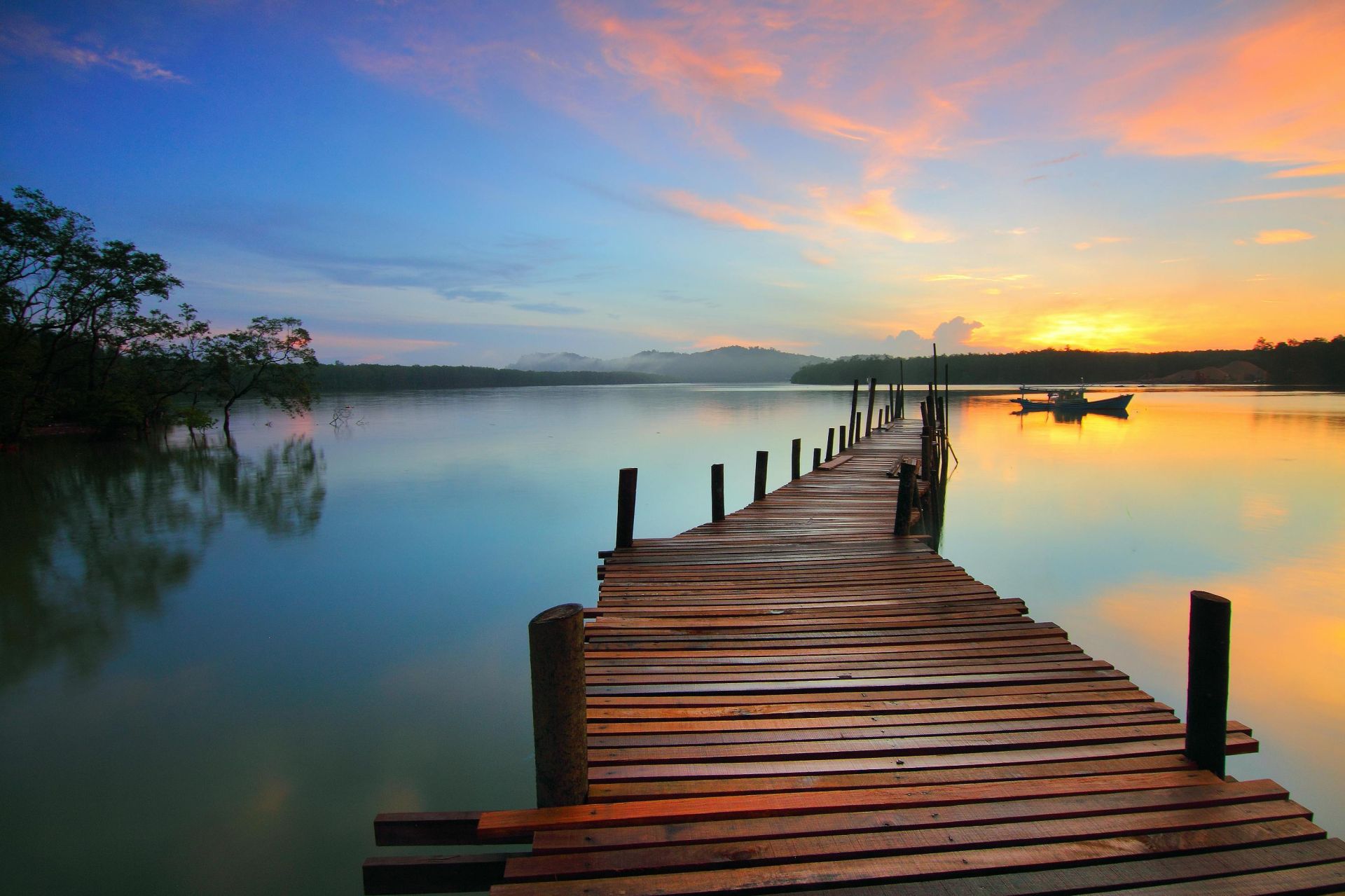 Serene sunset view over a tranquil lake with a wooden dock stretching into the distance.