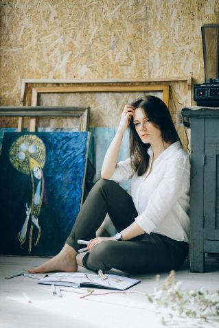 A woman sitting in an art studio, surrounded by paintings, deep in contemplation.