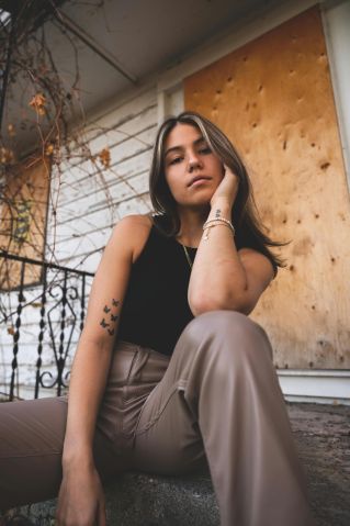 Stylish woman posing on steps, capturing a moment of reflection against a rustic background.